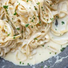 pasta with white sauce and parsley in a black bowl on top of a table