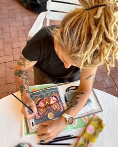 a woman sitting at a table working on some artwork