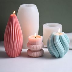 three different colored vases sitting next to each other on a white table top with candles in them