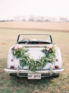 an old car decorated with flowers and greenery is parked on the grass in front of a field