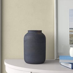 a black vase sitting on top of a white table next to a book and candle