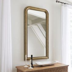 a large mirror sitting on top of a wooden dresser next to a white curtained window