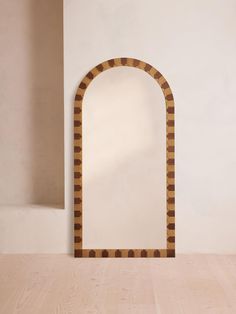 an arch shaped mirror sitting on top of a wooden floor next to a white wall