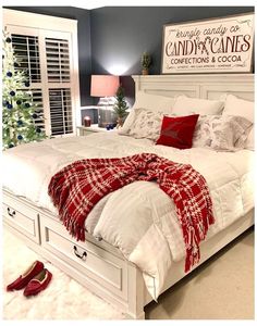 a white bed with red pillows and blankets on it in front of a christmas tree