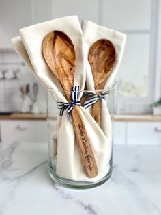 two wooden spoons are wrapped in white paper and tied with blue ribbon on a marble countertop