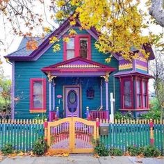 a blue house with red and yellow trim on the front door is surrounded by autumn leaves