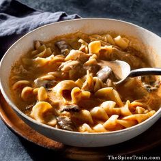 a white bowl filled with pasta and meat soup on top of a wooden plate next to a gray napkin