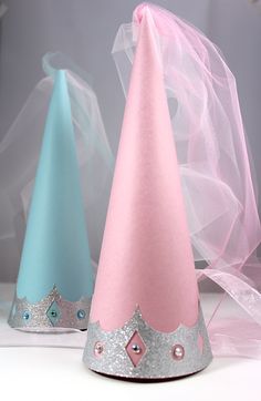 two party hats sitting next to each other on top of a white table with pink and blue ribbons