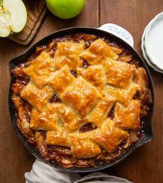 an apple pie in a cast iron skillet on a wooden table next to apples