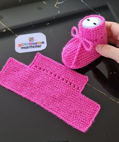 a hand holding a pink knitted object next to a sticker with the word mother written on it