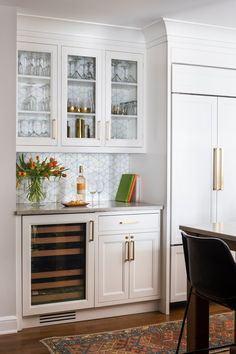 a kitchen with white cabinets and glass front cupboards on the wall, including a wine cooler