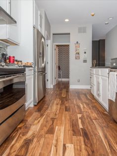 an empty kitchen with wood floors and stainless steel appliances in the middle of the room