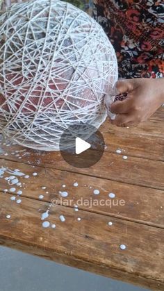 a person is holding a ball of yarn on a wooden table with white stuff all over it