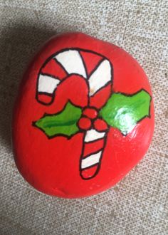 a painted rock with candy canes and holly on it, sitting on the ground