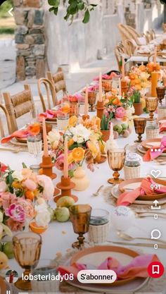 a long table is set with orange and pink flowers, plates and utensils