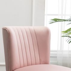 a pink velvet chair next to a potted plant