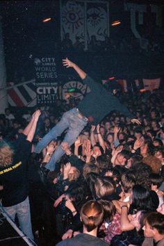 a crowd of people at a concert with their arms in the air and one person jumping up into the air