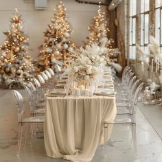 a table set up for a formal event with white flowers and candles on it, surrounded by christmas trees