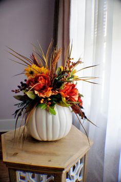 a white pumpkin shaped vase filled with flowers on top of a wooden table next to a window