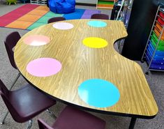 a wooden table topped with lots of different colored chairs