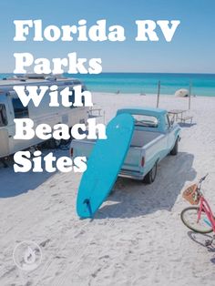 a blue surfboard sitting on top of a beach next to a parked truck and camper