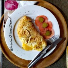 a white plate topped with an omelet next to a fork and knife on top of a table