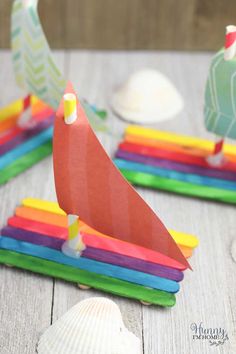 colorful paper boats sitting on top of a wooden table next to shells and seashells