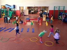 children are playing in an indoor play area with colorful obstacles and rings on the floor