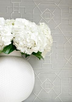 a white vase filled with flowers on top of a wooden table next to a wall