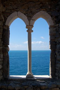 an open window with a view of the ocean and sky from inside a stone building