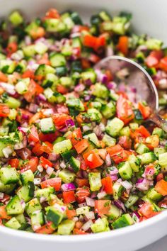 a white bowl filled with cucumber, red onion and tomato salad next to a wooden spoon