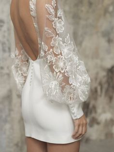 the back of a woman wearing a white dress with sheer sleeves and flowers on it