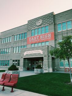 two red benches sitting in front of a large building with a clock on it's side