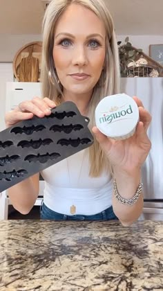 a woman holding up a doughnut in front of a cookie sheet with bats on it