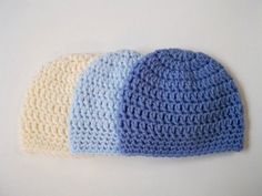 three crocheted hats sitting next to each other on a white surface, one blue and one beige