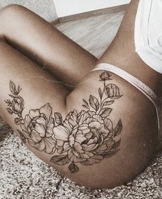 a woman laying on the floor with flowers tattooed on her thigh and leg behind her