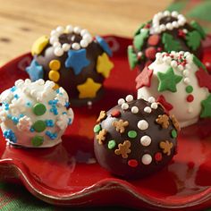 four chocolate covered desserts on a red plate with green and white decorations around them