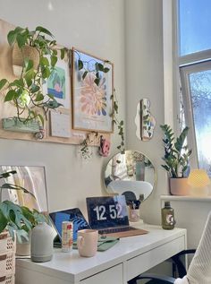 a white desk topped with a laptop computer next to a plant filled window sill