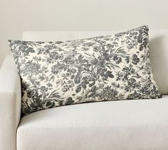 a white couch with a black and white floral pillow sitting on it's back