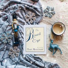 a book and toy on a blanket with snowflakes around it, next to a cup of tea