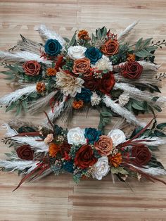 an arrangement of flowers and feathers on a wooden floor in the shape of a wreath