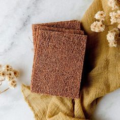 two pieces of brown paper sitting on top of a table next to dried flowers and a cloth