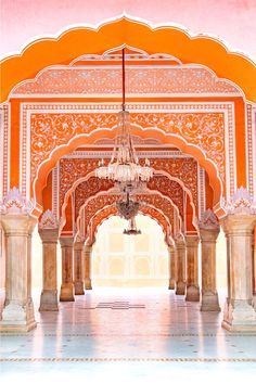 an ornate archway with chandelier and pillars in front of a pink sky background