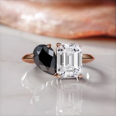 an emerald and black diamond engagement ring on a white surface with a large piece of jewelry in the background