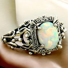 Introducing a stunning piece of history and craftsmanship: our Vintage Estate Lab Created Cabochon Opal Solitaire Filigree Ring. This exquisite ring is meticulously crafted from solid 925 sterling silver, showcasing the timeless beauty of filigree work that adds intricate elegance to any outfit. The centerpiece of this enchanting ring is a high-quality lab created opal stone, measuring 8x6 mm, which radiates hues of mesmerizing blue and green, mirroring the shimmering depths of the ocean. With the top of the ring measuring nearly 1/2 inch in length, it's a standout piece that draws admiration without being overwhelming. Not only does this ring embody vintage glamour, but it also represents a commitment to sustainability. This stunning ring is stamped with "925," ensuring you receive authen Vintage White Jewelry For Ceremonial Occasions, Classic Wedding Jewelry With Cabochon, Heirloom Jewelry With Intricate Design For Collectors, Classic Cabochon Opal Ring For Anniversary, White Heirloom Jewelry For Ceremonial Occasions, Heirloom White Jewelry For Ceremonial Occasion, Antique Cabochon Opal Ring For Anniversary, Antique Opal Cabochon Ring For Anniversary, Victorian Oval Opal Ring For Anniversary