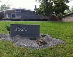 the address sign is displayed in front of a house with grass and rocks around it