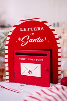 a red letter to santa mailbox sitting on top of a table next to candy canes