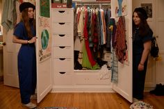 two women standing in front of a closet with clothes hanging on the shelves and drawers