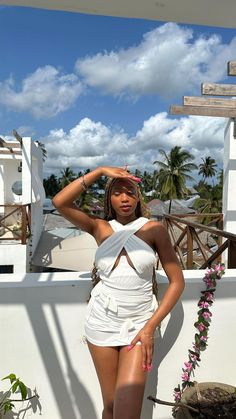 a woman in a short white dress posing for the camera with her hand on her head