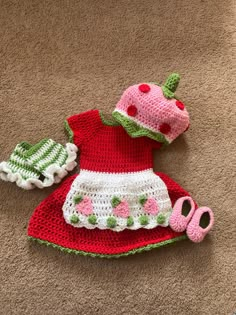 a crocheted strawberry hat and booties are laying on the floor